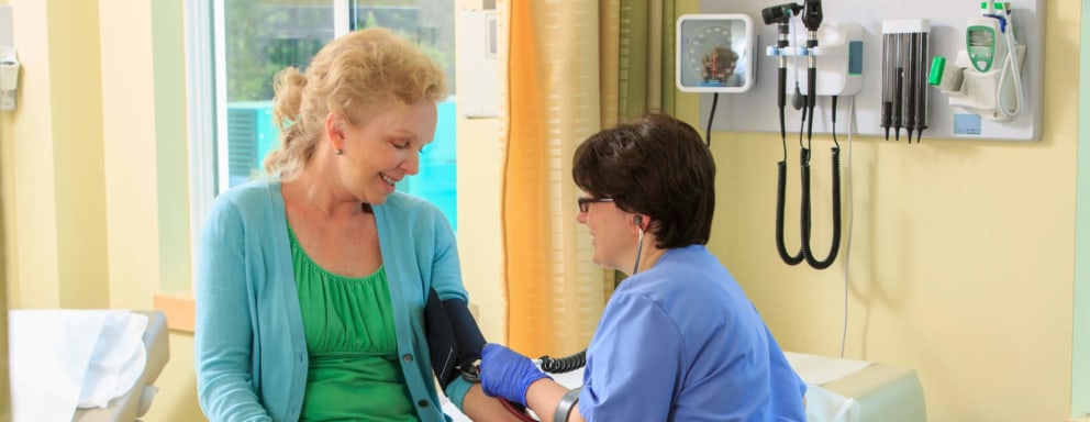 Female nurse using walking canes measures a senior patient's blood pressure in a clinical office room.